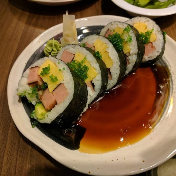 Chopstix 2 sushi rolls with spam, egg, avocado, and green tobiko, served with soy sauce.