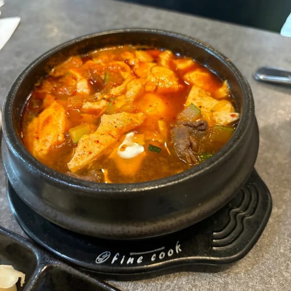 Spicy Korean tofu stew with meat and vegetables in a black stone pot on a gray table.