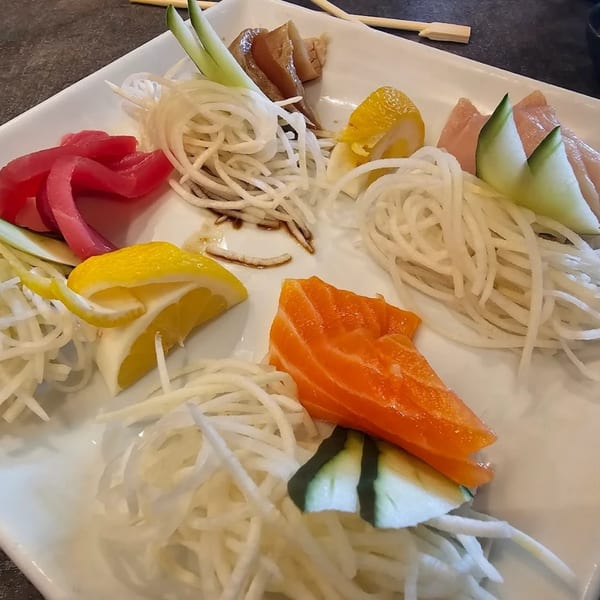 A white plate of Chopstix 2 sashimi with tuna, salmon, and other fish, garnished with daikon and lemon.