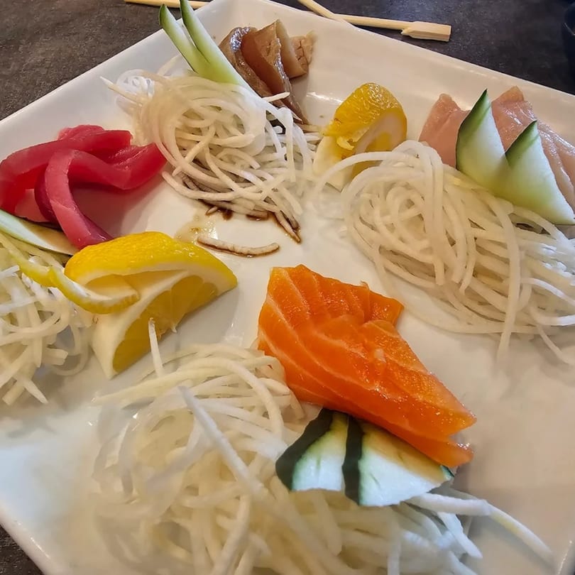 A white plate of Chopstix 2 sashimi with tuna, salmon, and other fish, garnished with daikon and lemon.