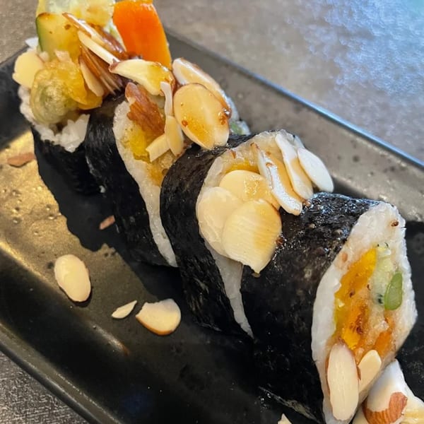 Chopstix 2 sushi rolls with rice, nori, vegetables, and sliced almonds on a black plate.