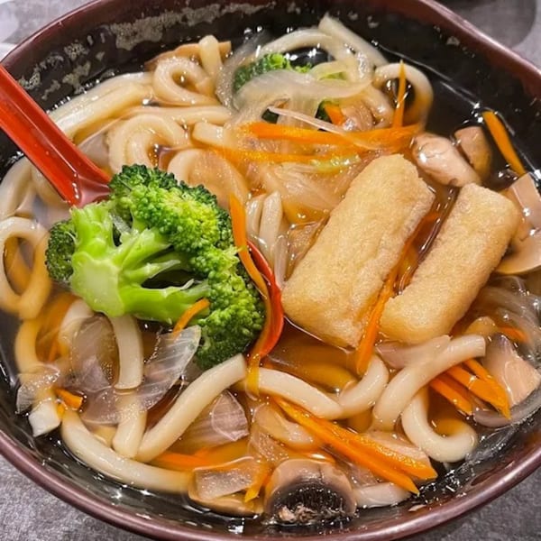 A bowl of Chopstix 2 udon noodle soup with broccoli, carrots, onions, mushrooms, and fried tofu.
